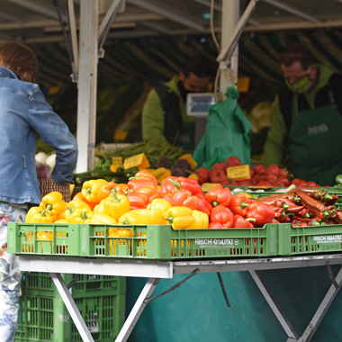 Kunden an einem Gemüsestand auf einem Wochenmarkt